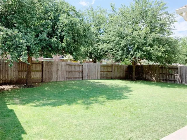 a view of a backyard with large trees and wooden fence