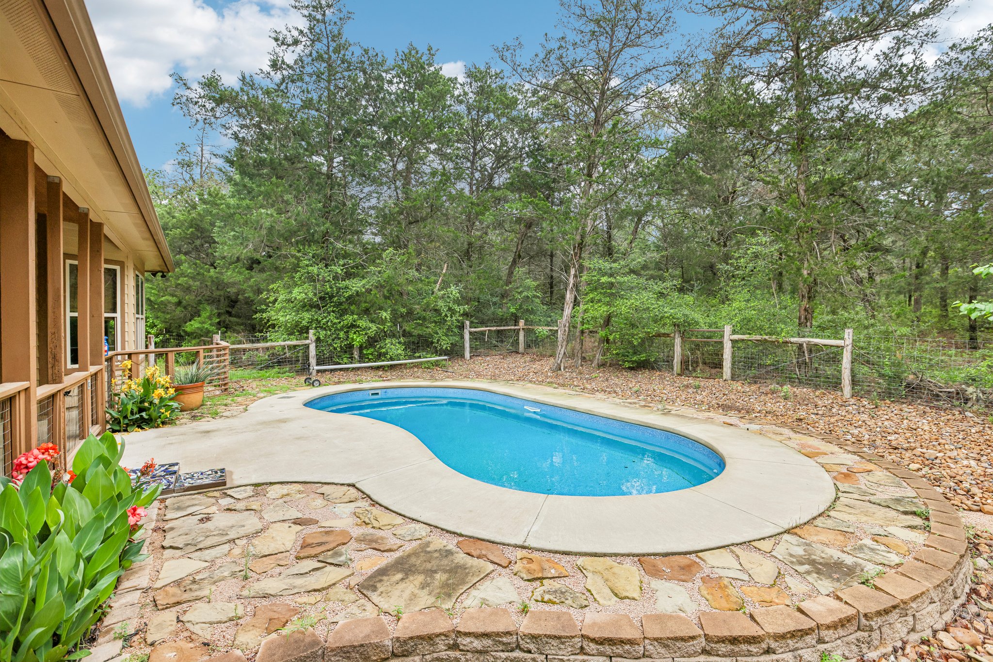 267 Corral Road Smithville, TX 78957 - Photo 37 of 40 Kidney-shaped swimming pool featuring concrete decking, a flagstone patio, and a stone retaining wall