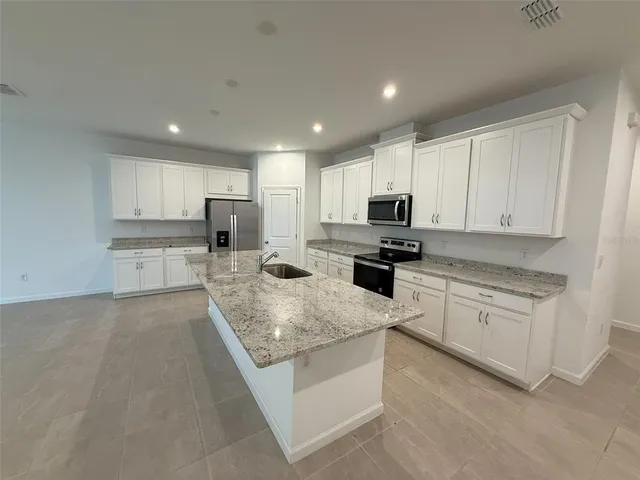 a kitchen with stainless steel appliances granite countertop a stove top oven a sink a refrigerator and white cabinets