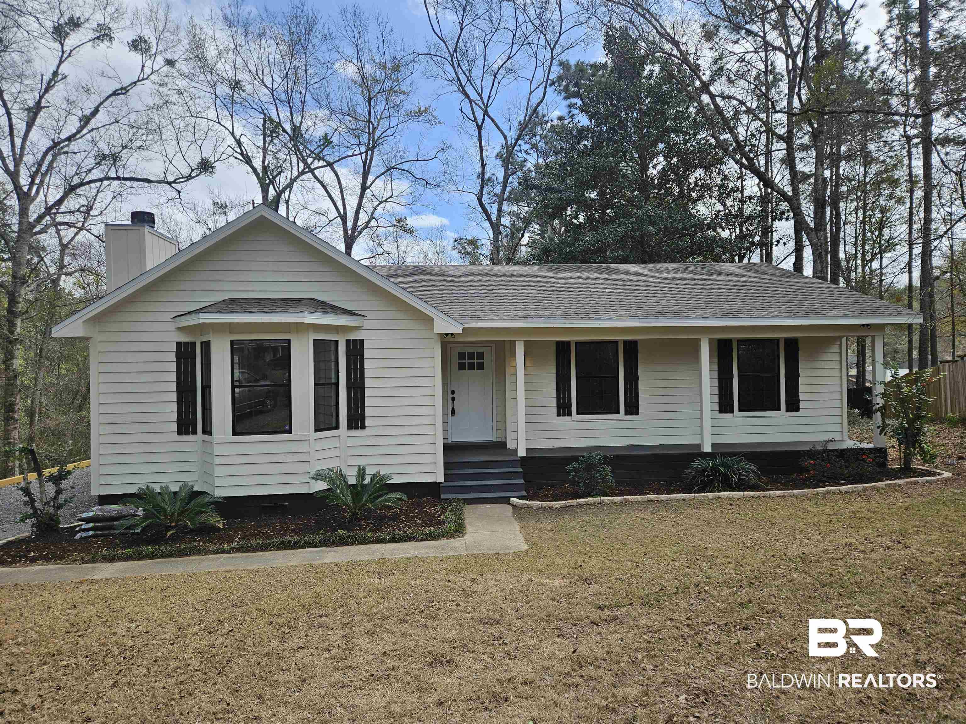 View of front of house with covered porch, a chimney, a front yard, and a shingled roof