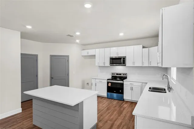 a kitchen with stainless steel appliances kitchen island a sink dishwasher a stove and a refrigerator with wooden floor