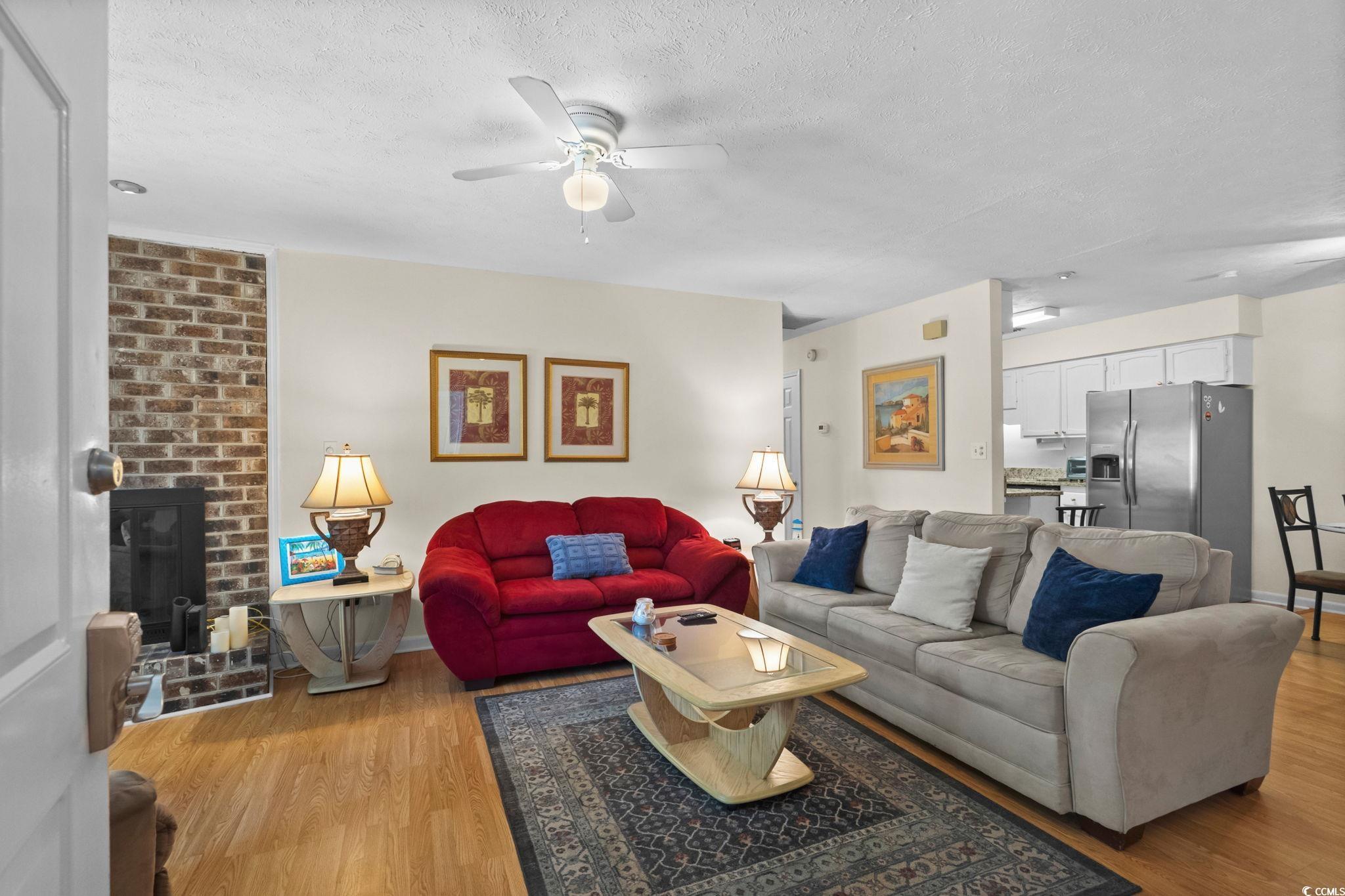 406 75th Avenue North, Unit Q Myrtle Beach, SC 29572 - Photo 3 of 23 Living area featuring light wood finished floors, a fireplace, a textured ceiling, and a ceiling fan