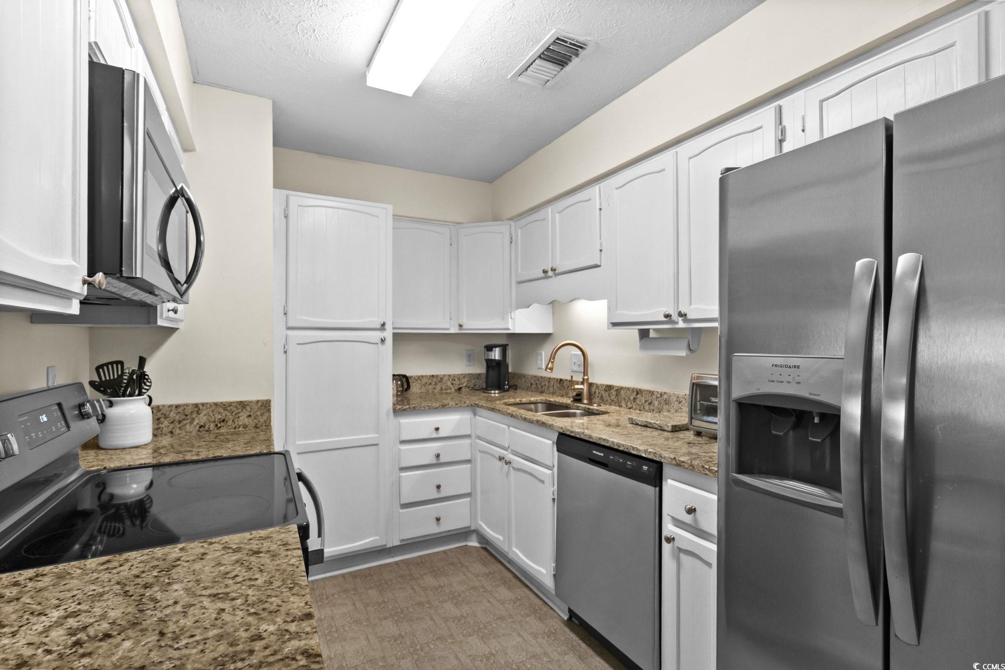 406 75th Avenue North, Unit Q Myrtle Beach, SC 29572 - Photo 8 of 23 Kitchen featuring appliances with stainless steel finishes, a textured ceiling, light stone countertops, and white cabinets