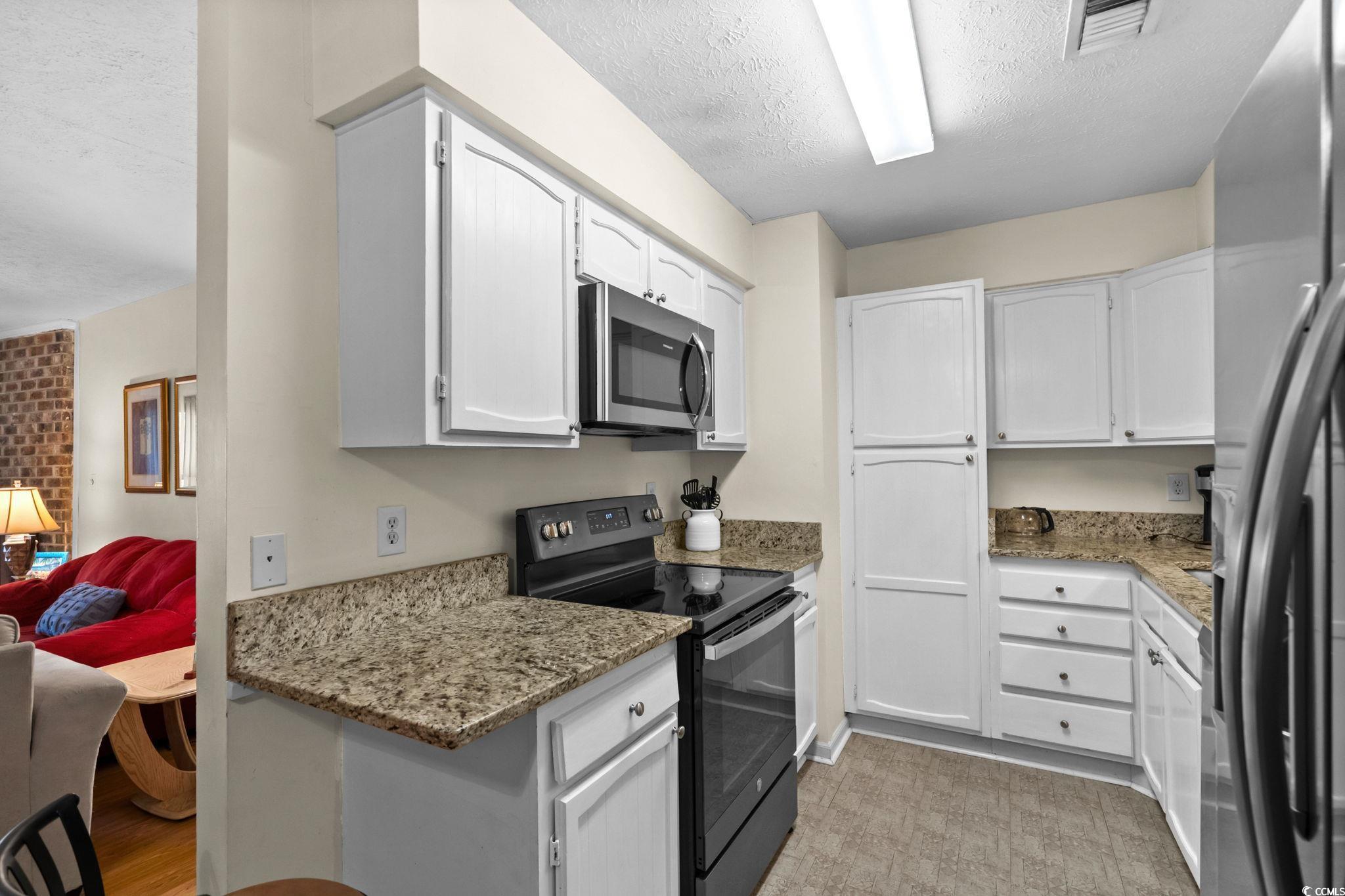 406 75th Avenue North, Unit Q Myrtle Beach, SC 29572 - Photo 9 of 23 Kitchen with stainless steel appliances, a textured ceiling, light stone counters, and white cabinets