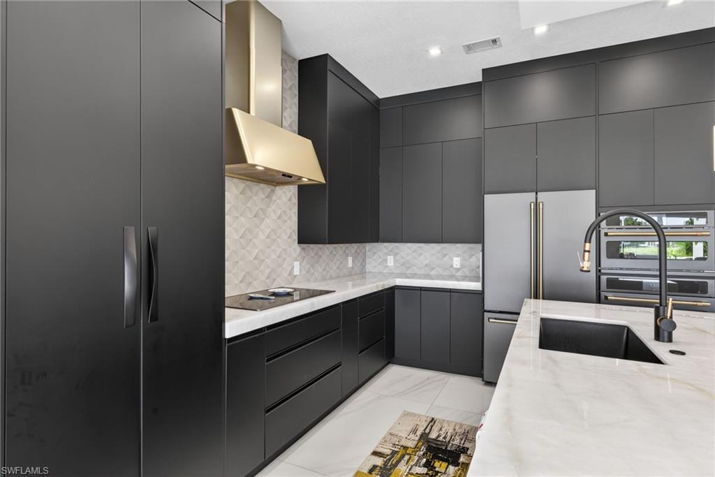 3956 Isla Ciudad Court Naples, FL 34109 - Photo 4 of 39 Kitchen with modern cabinets, wall chimney exhaust hood, light stone countertops, built in refrigerator, and tasteful backsplash