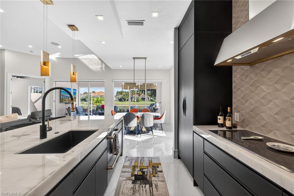 3956 Isla Ciudad Court Naples, FL 34109 - Photo 5 of 39 Kitchen with dark cabinets, backsplash, pendant lighting, and wall chimney range hood