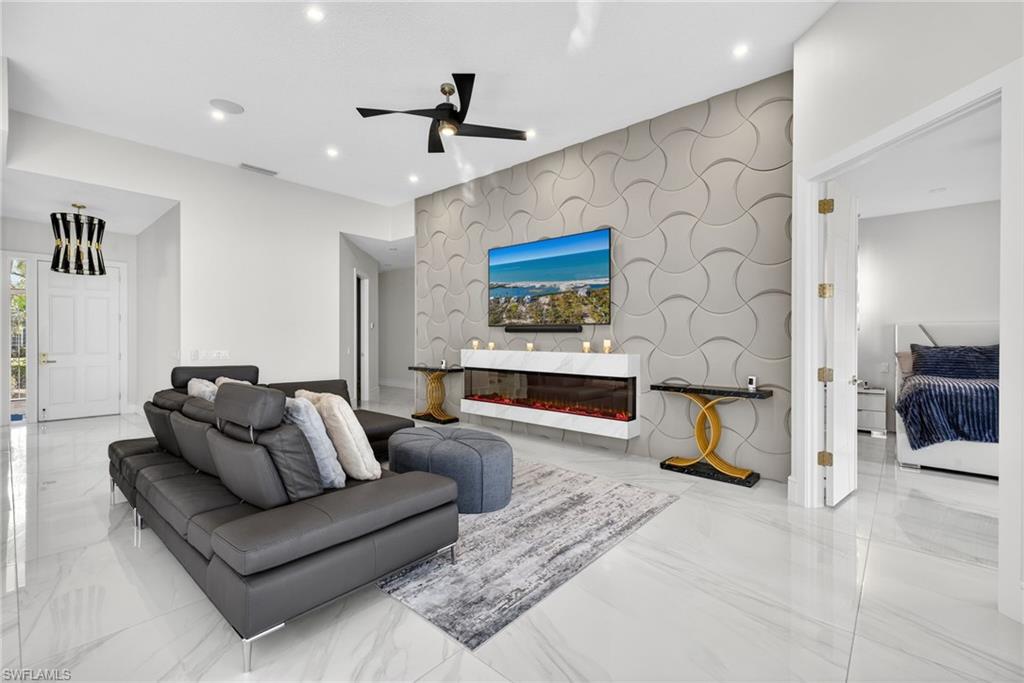 3956 Isla Ciudad Court Naples, FL 34109 - Photo 8 of 39 Living room featuring an accent wall, a ceiling fan, light marble finish flooring, recessed lighting, and a glass covered fireplace