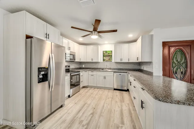 a kitchen with stainless steel appliances granite countertop a refrigerator a sink dishwasher a stove and white countertops with wooden floor