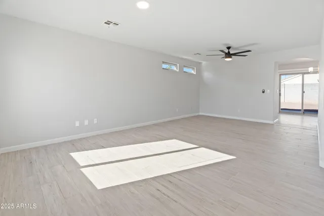 an empty room with wooden floor ceiling fan and windows