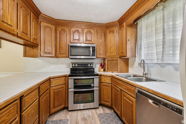 553 North 200 West Bountiful, UT 84010 - Photo 8 of 26 Kitchen with light countertops, wood finish cabinetry, stainless steel appliances, a textured ceiling, and light wood finished floors