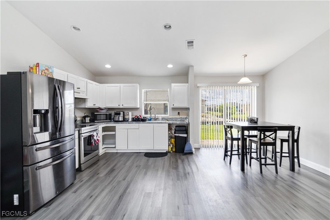 776-778 Alabama Road South Lehigh Acres, FL 33974 - Photo 16 of 50 a kitchen with a refrigerator a kitchen island a stove a table and chairs with wooden floor