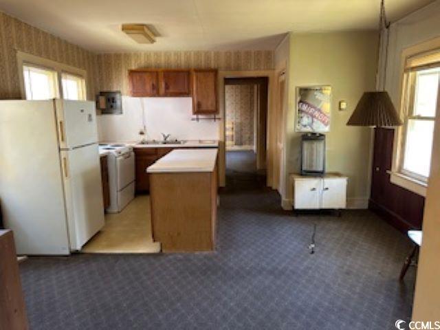 Kitchen featuring light countertops, freestanding refrigerator, carpet, brown cabinets, and electric range
