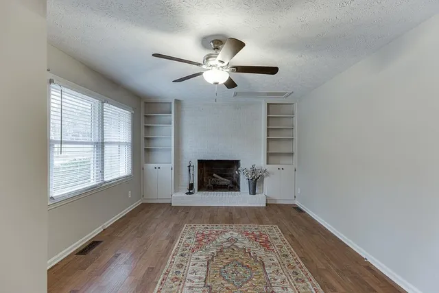 a view of a livingroom with a fireplace a ceiling fan and windows