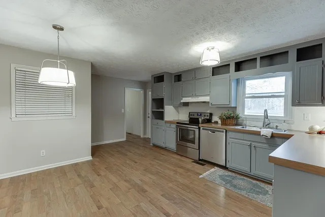 a kitchen with a stove a sink dishwasher a refrigerator and white cabinets with wooden floor