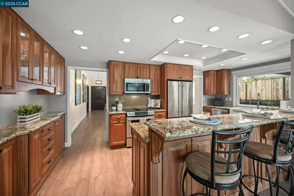 a kitchen with stainless steel appliances kitchen island granite countertop a stove top oven a refrigerator a sink and a dining table with wooden floor