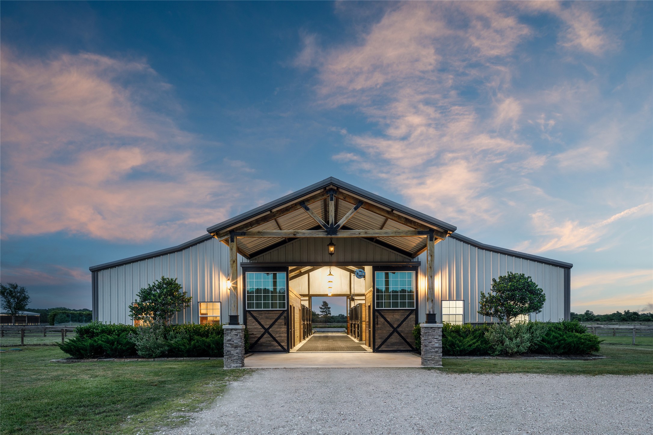 24118 Margerstadt Road Hockley, TX 77447 - Photo 4 of 49 Positioned at the center of the equestrian facilities, the fully insulated horse barn combines oversized stalls, breezeway airflow, climate-controlled tack spaces, and integrated utility areas within a clean and refined layout. Warm lighting and symmetrical architecture give the structure a strong presence across the surrounding acreage.