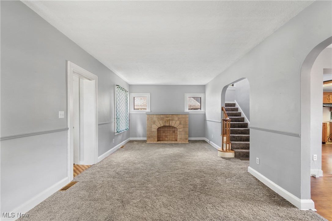 302 Poplar Avenue Northwest Canton, OH 44708 - Photo 5 of 34 Unfurnished living room featuring arched walkways, a fireplace, carpet flooring, and stairs