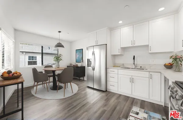 a kitchen with stainless steel appliances granite countertop a dining table chairs refrigerator and sink