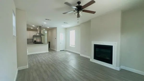 an empty room with wooden floor a ceiling fan a fireplace and windows