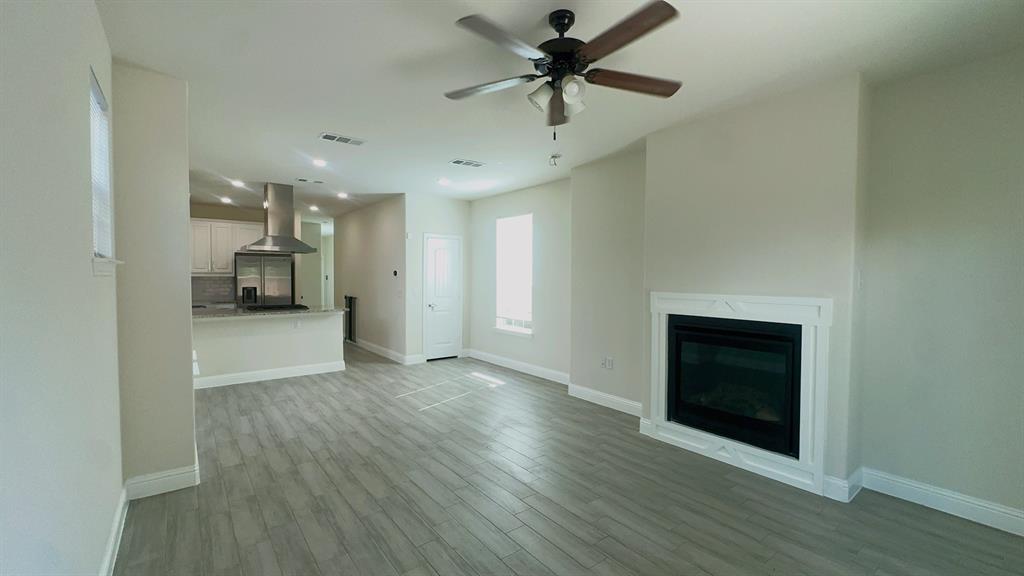 2239 Anderson Street Dallas, TX 75215 - Photo 6 of 16 an empty room with wooden floor a ceiling fan a fireplace and windows