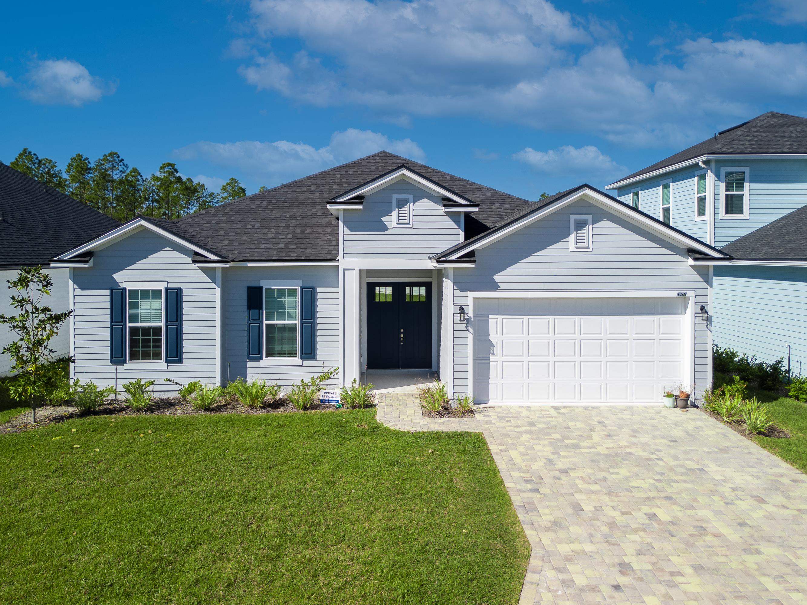 Traditional-style house featuring decorative driveway, roof with shingles, an attached garage, and a front lawn
