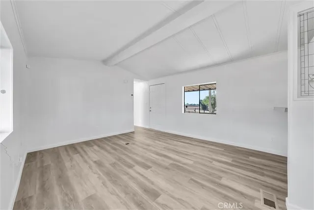 a view of empty room with wooden floor and kitchen view