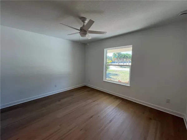 an empty room with wooden floor fan and windows