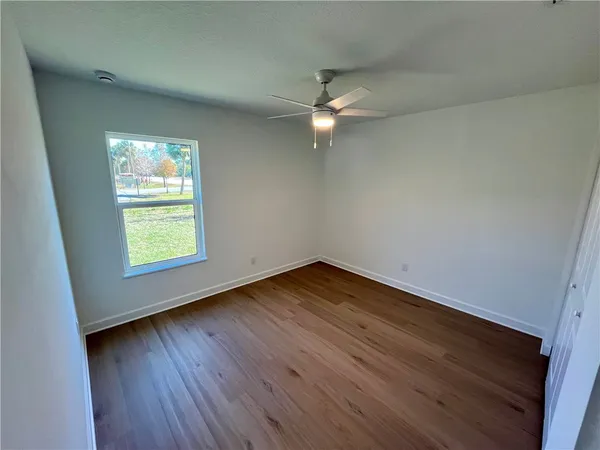 an empty room with wooden floor fan and windows