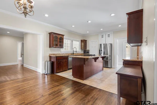 a large kitchen with stainless steel appliances granite countertop a stove a sink dishwasher a microwave oven and a dining table with wooden floor
