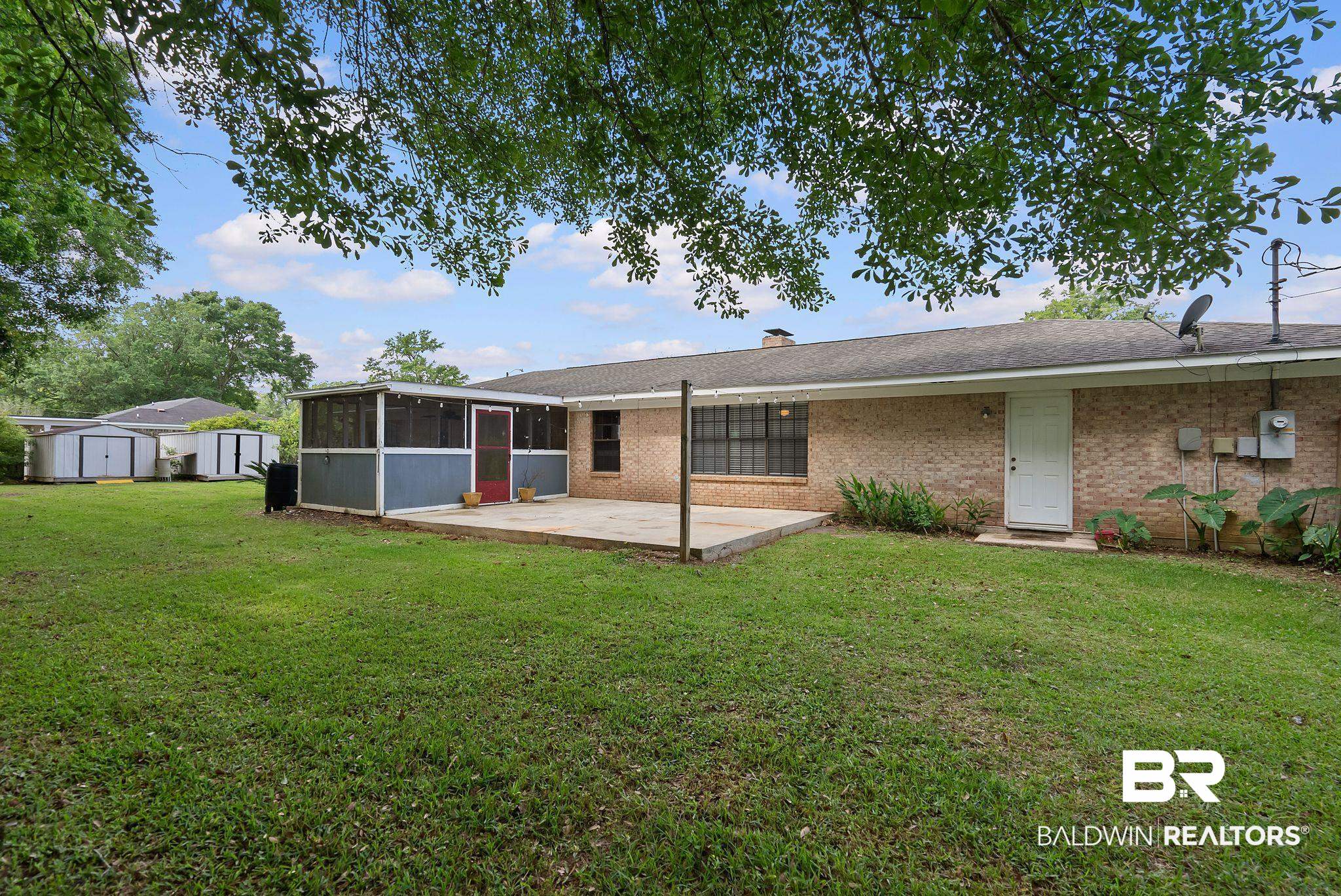716 North Cedar Street Foley, AL 36535 - Photo 22 of 25 Expansive backyard featuring a screened-in patio, concrete slab patio, and two storage sheds