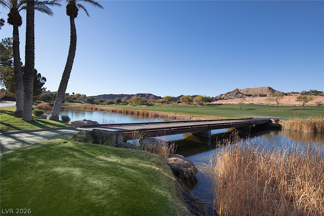 25 Falling Ridge Lane Henderson, NV 89011 - Photo 43 of 48 Experience tranquil golf course living with a scenic bridge crossing a peaceful pond, framed by towering palms and distant mountains.