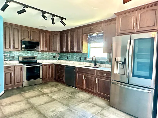 a large kitchen with stainless steel appliances granite countertop a stove top oven a refrigerator and a sink