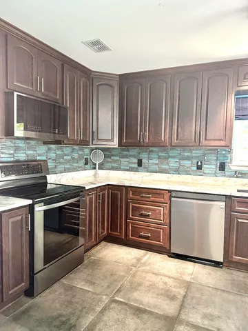 a kitchen with stainless steel appliances granite countertop a sink a stove a refrigerator cabinets and a window