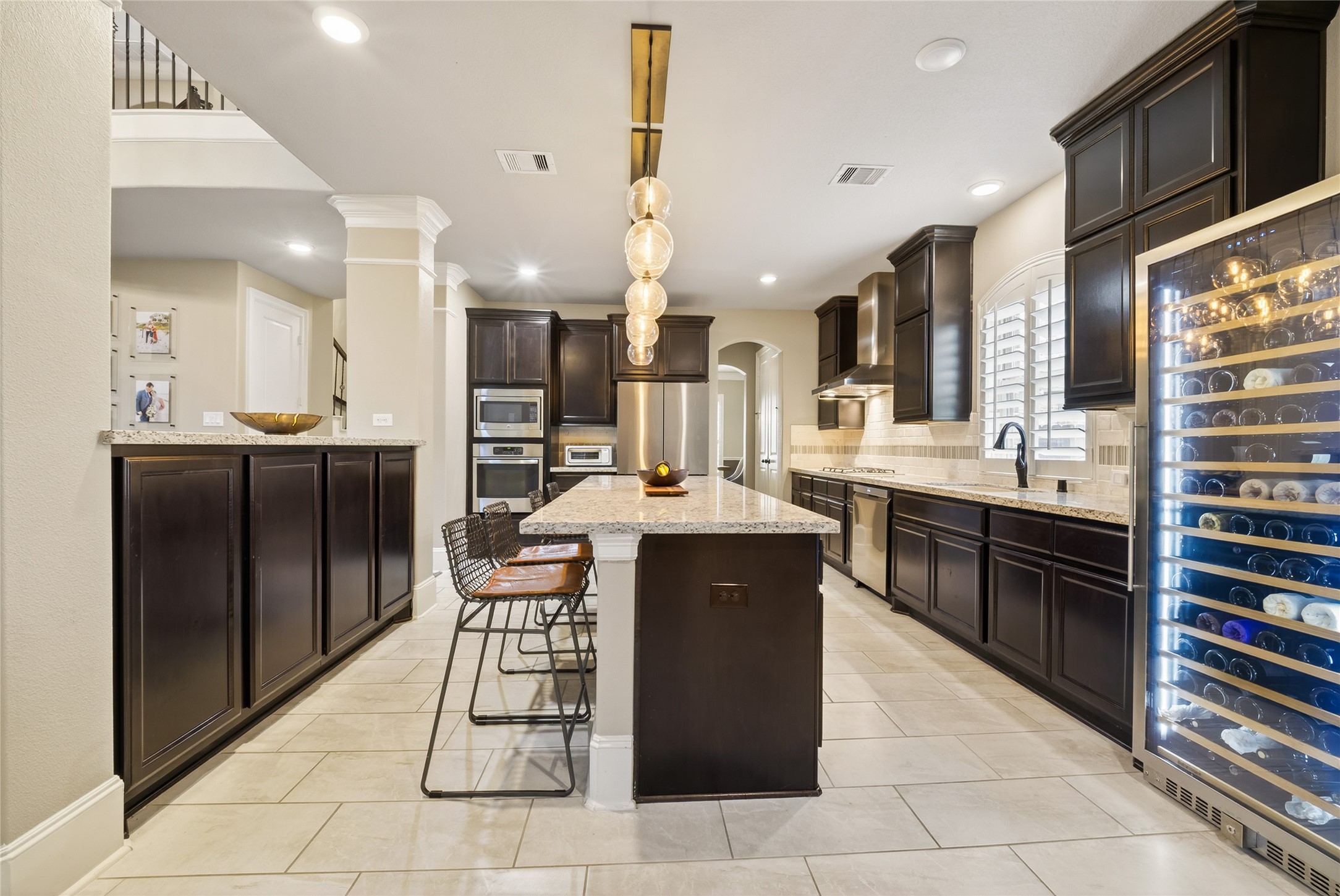 7907 Augusta Creek Court Spring, TX 77389 - Photo 14 of 49 This modern kitchen features dark wood cabinetry, a large central island with seating, stainless steel appliances. The space is well-lit with recessed lighting and designer inspired pendant fixtures, and offers ample counter space with a sleek, open design.