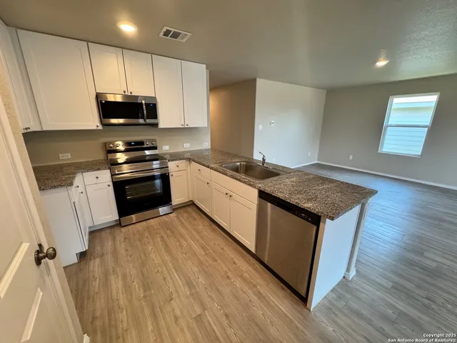 a kitchen with stainless steel appliances granite countertop a stove top oven a sink dishwasher and a microwave oven on the wooden floor