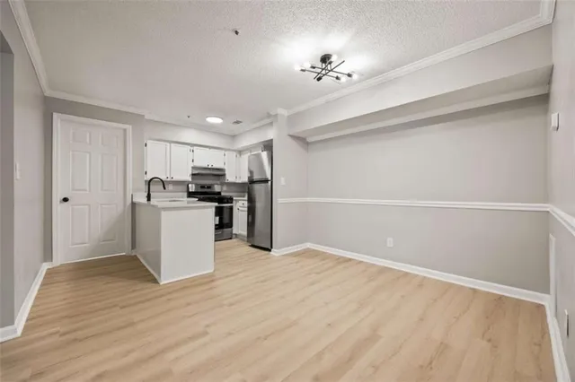 a view of an empty room with kitchen and wooden floor