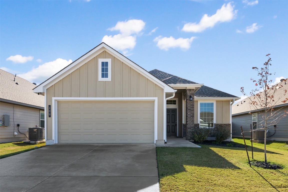 View of front of property featuring board and batten siding, a shingled roof, brick siding, a front lawn, and concrete driveway