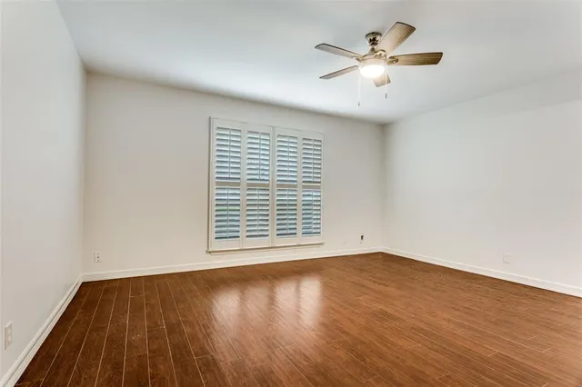 a view of an empty room with wooden floor and a ceiling fan