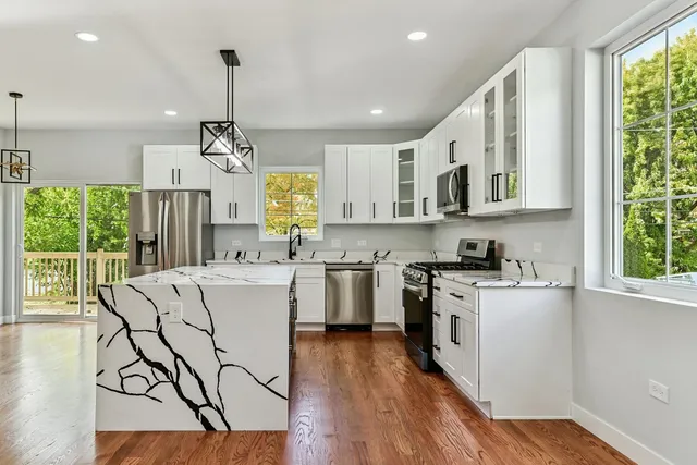 a kitchen with stainless steel appliances a stove a sink dishwasher a refrigerator white cabinets and wooden floor next to a window