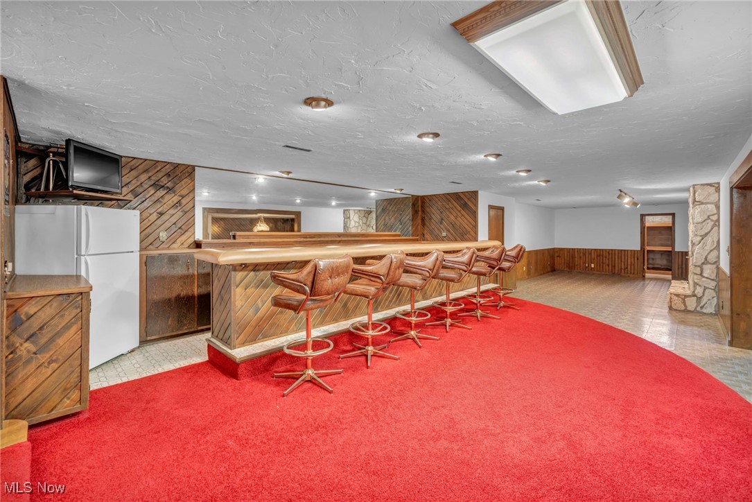36350 Bainbridge Road Solon, OH 44139 - Photo 20 of 38 Bar with a textured ceiling, white refrigerator, light colored carpet, and wooden walls