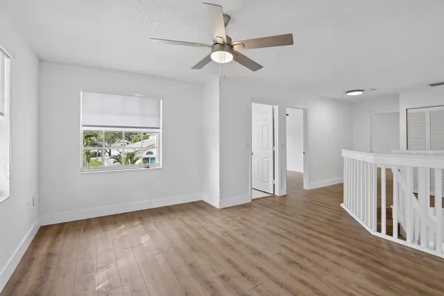 an empty room with wooden floor chandelier fan and windows