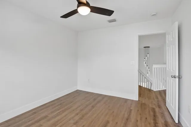 an empty room with wooden floor ceiling fan and windows