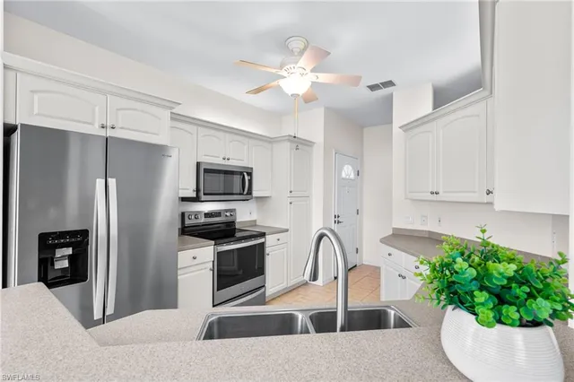 a kitchen with stainless steel appliances kitchen island granite countertop a refrigerator a stove a microwave oven a sink with white cabinets and wooden floor