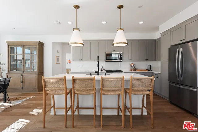 a kitchen with stainless steel appliances kitchen island granite countertop a dining table chairs and a refrigerator