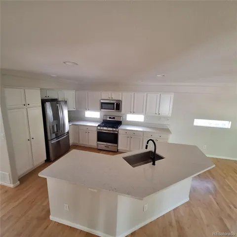 a kitchen with stainless steel appliances a sink a stove a refrigerator cabinets and wooden floor