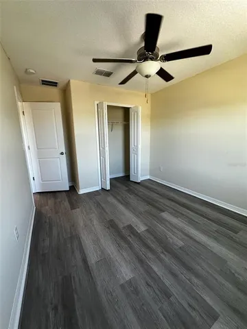 a view of an empty room with wooden floor and a ceiling fan