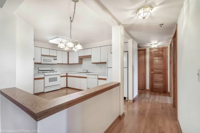 a kitchen with stainless steel appliances granite countertop a sink dishwasher a refrigerator and white cabinets with wooden floor