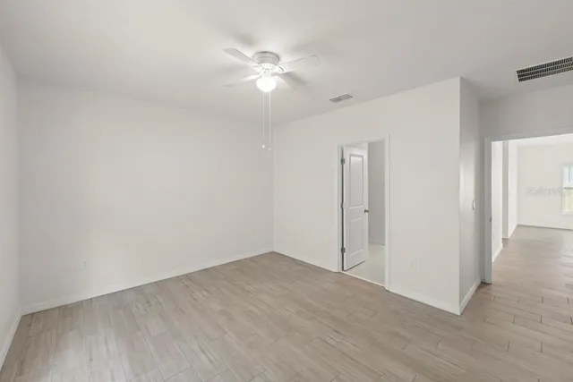 an empty room with wooden floor and fan