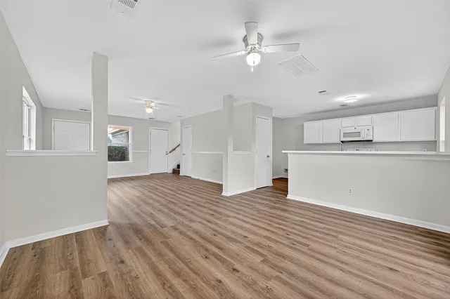 an empty room with wooden floor chandelier fan and windows