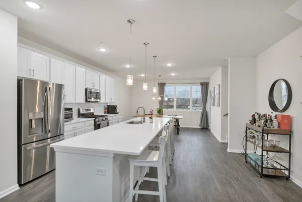 a kitchen with stainless steel appliances a refrigerator a stove a sink dishwasher a dining table and chairs with wooden floor